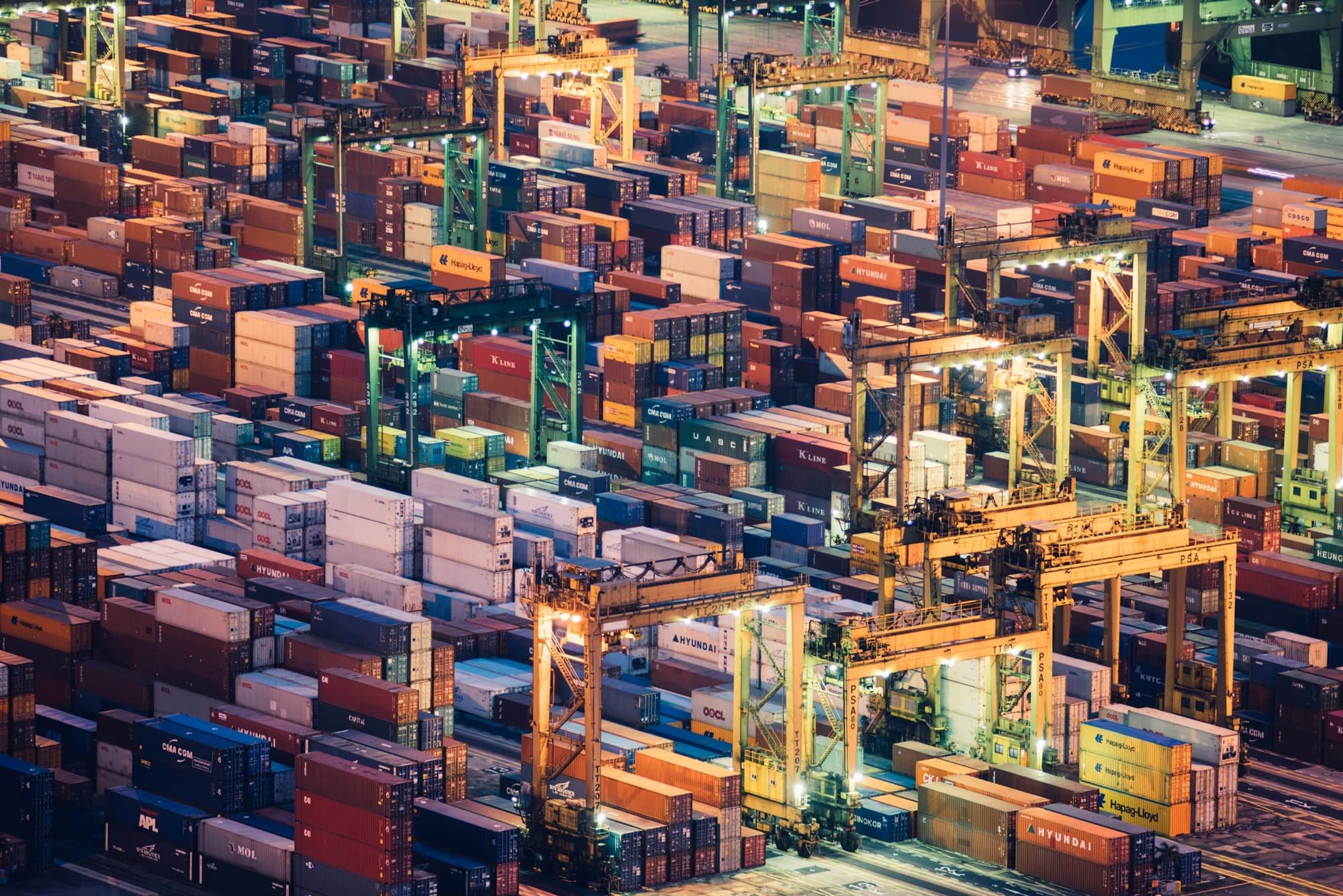 A container port at night, seen as a dense grid of moving global trade